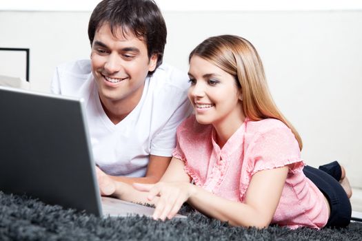 Happy young couple using laptop on floor of room.