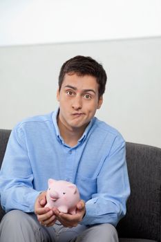 Portrait of young businessman making a face while holding piggybank