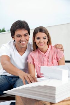 Happy young couple in casuals looking at an architectural model structure