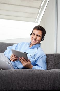 Portrait of happy young man in formal wear listening to music on digital tablet
