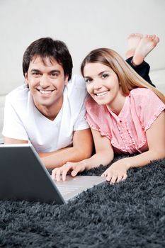 Happy young couple using laptop, looking at camera.