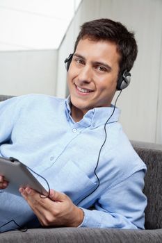Portrait of handsome young man in formal shirt listening to music on digital tablet
