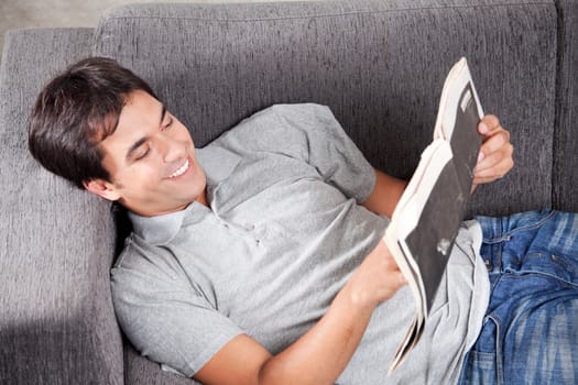 Happy young man reading newspaper on couch.