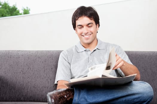 Happy young man reading newspaper on couch.