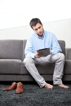 Young man using digital tablet at home on couch.