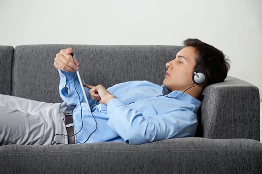 Relaxed young man in formal wear browsing internet while listening to music on digital tablet