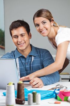 Portrait of young female fashion designer assisting man while working on laptop