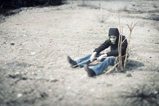 Single human in gas mask sitting in the desert near the dead plant. Concept of the futuristic environmental disaster. Special color added and shallow depth of field due to the tilt/shift lens for movie effect