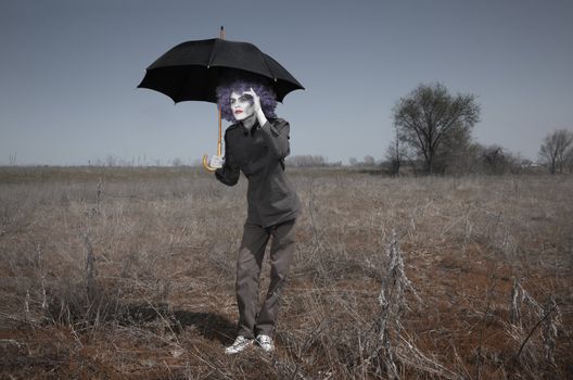 Funny man in the steppe holding umbrella and looking beyond the horizon. Artistic darkness and colors added