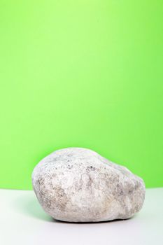 Single waterworn smooth white rock standing on a white countertop against a green background with copyspace