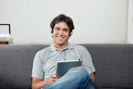 Portrait of happy young man in casual wear listening music on tablet PC