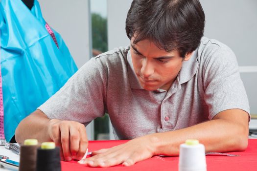 Young male dressmaker drawing line on a red fabric with chalk