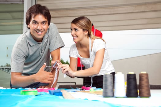 Portrait of male tailor with female assistant cutting ribbon