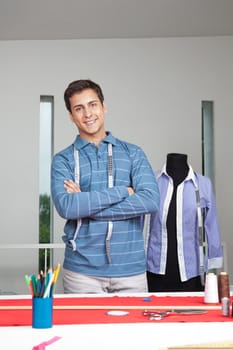 Portrait of young male tailor standing arms crossed with mannequin in background