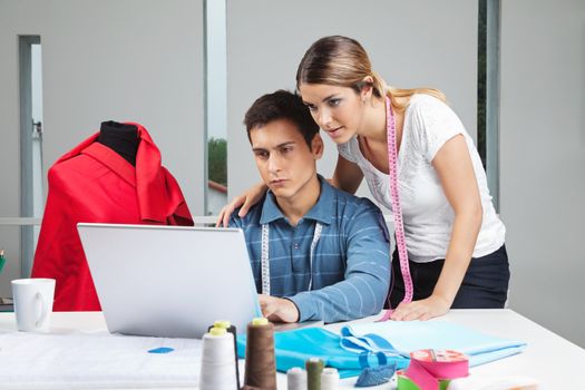 Young clothing designers working on laptop together in workshop