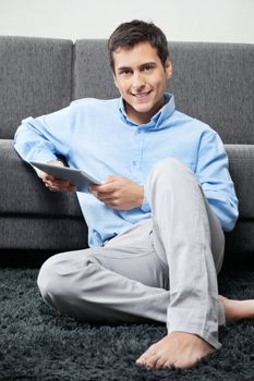 Portrait of young man in formal wear sitting comfortably on rug with digital tablet
