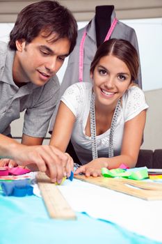 Portrait of young female fashion designer smiling while coworker draws line on fabric with chalk