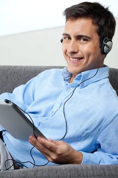 Portrait of relaxed young man smiling while listening music on digital tablet
