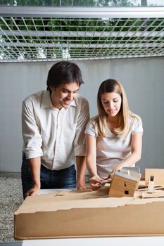 Young male architect standing beside colleague working on model house