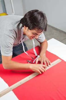 Young male dressmaker measuring a red fabric with ruler on table
