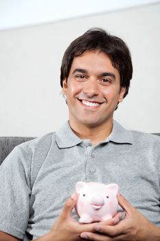 Portrait of young man in casual grey t-shirt smiling while holding piggybank