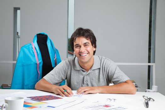 Portrait of happy young dressmaker working on rough outline designs at workshop