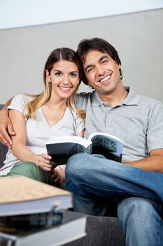 Portrait of happy young couple sitting together on sofa with a book
