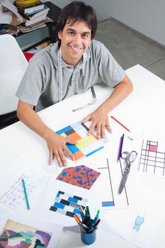 High angle view of male fashion designer sitting at table with outline designs and patterns at workshop