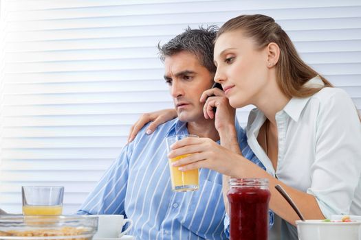 Mid adult man on call while woman beside him holding glass of orange juice