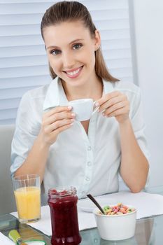 Portrait of a beautiful young woman having tea with juice, jam jar and cereal bowl at table