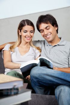 Happy young couple reading book together on sofa at home