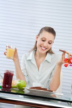 Happy young woman looking down at plate of bread slices while having orange juice