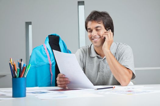 Young male clothing designer answering a phone call while holding paper