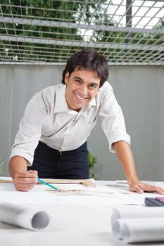 Portrait of young male architect smiling while working on blueprint