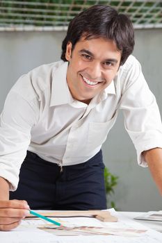 Portrait of young male architect smiling while working on blueprint