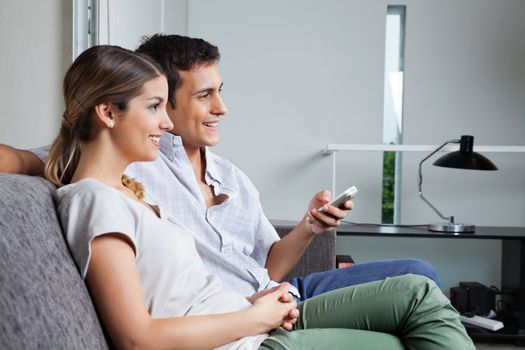 Man holding remote control while sitting with girlfriend at home