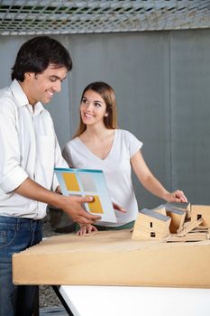 Young male architect looking at model house while female colleague smiling at him