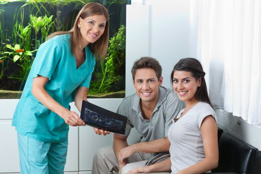 Portrait of a female dentist showing dental X-ray to young couple in clinic