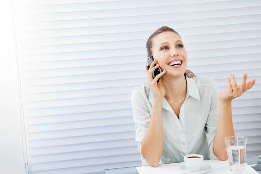 Happy young businesswoman answering phone call while sitting at table