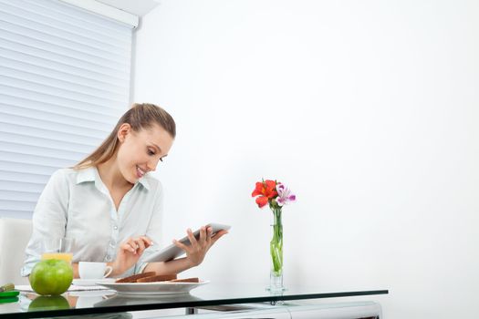 Happy young businesswoman browsing net on tablet PC while having breakfast