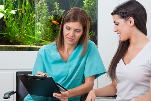 Young woman paying bill through credit card to female dentist in clinic