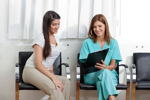 Female dentist showing something to young patient on clipboard in clinic