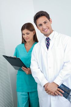 Portrait of happy male dentist with assistant holding clipboard in clinic