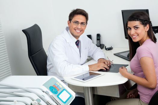 Portrait of happy young dentist and female patient sitting at office desk