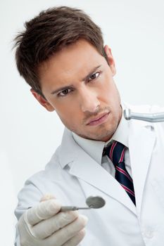 Portrait of young male dentist holding drill and angled mirror