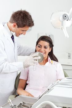 Young male dentist showing the result of his work to the satisfied patient