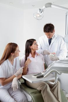 Male dentist explaining teeth model to patient while nurse looking at them in clinic