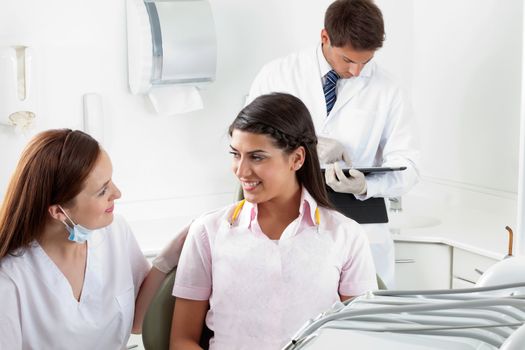 Nurse communicating with female patient while dentist using digital tablet in the background