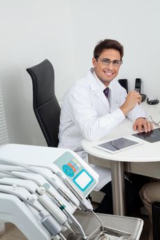 Portrait of a happy young male dentist sitting at office desk