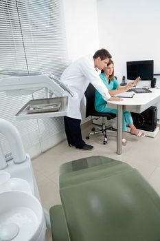 Doctor and female assistant in discussion with dentist chair in foreground